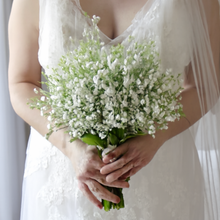 Bride holding a bouquet of white lily of the valley artificial flowers with a blurred background