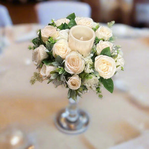 A table centrepiece of ivory flowers, foliage & led candle