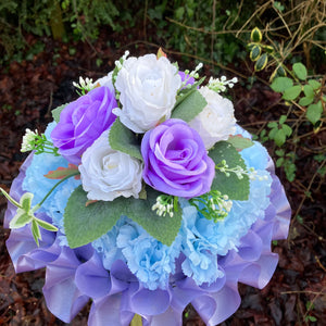 a funeral posy of artificial silk roses and lily flowers in shades of lilac and white