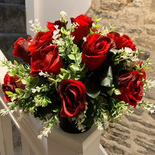 A graveside flower arrangement of roses and gyp in black pot