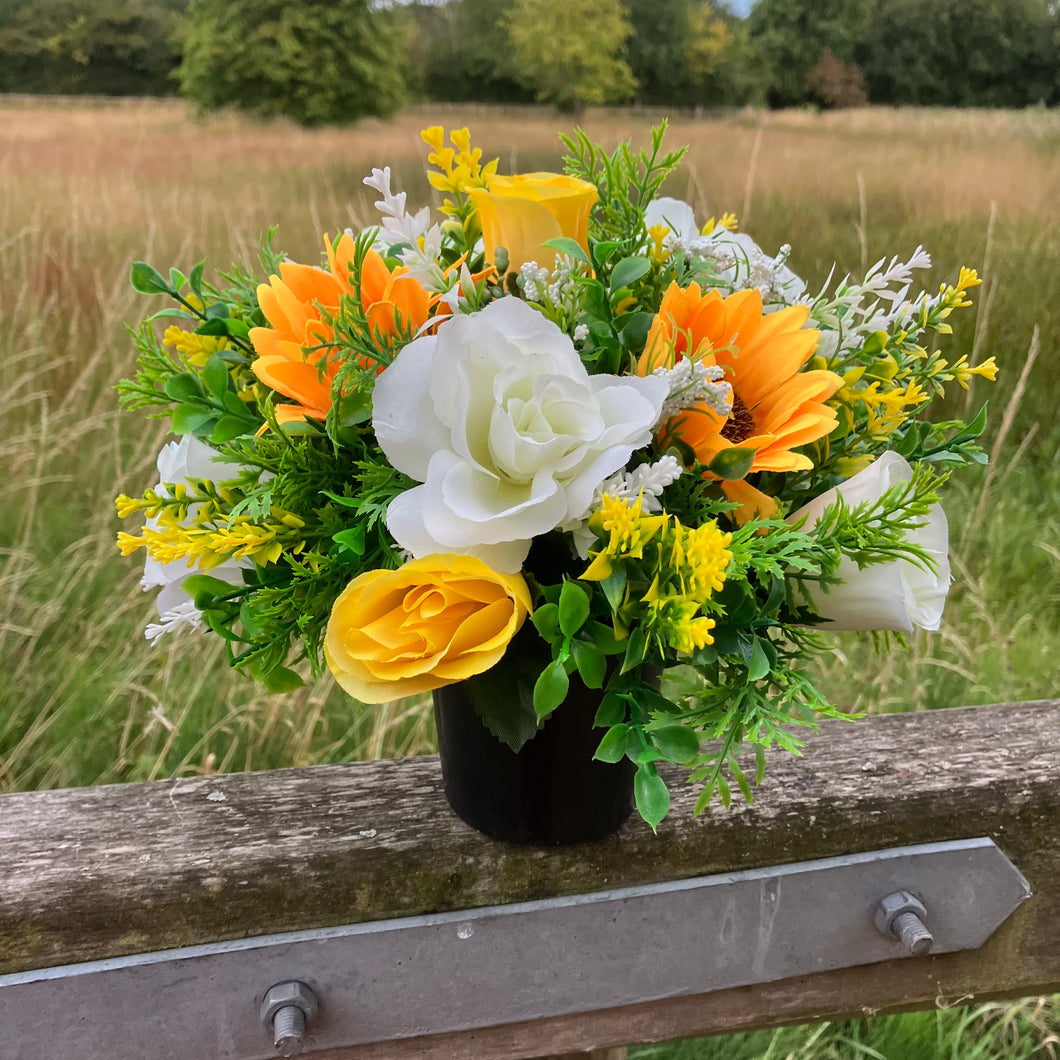 a grave side pot with flowers in shades of yellow and cream