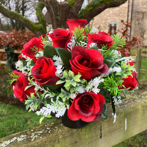 A graveside flower arrangement of roses and gyp in black pot