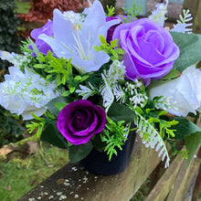 a graveside ivory and purple artificial memorial flower arrangement in black plastic pot