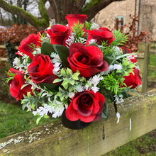 A graveside flower arrangement of roses and gyp in black pot