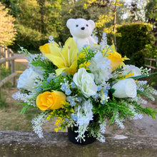 A graveside flower arrangement with teddy in black pot