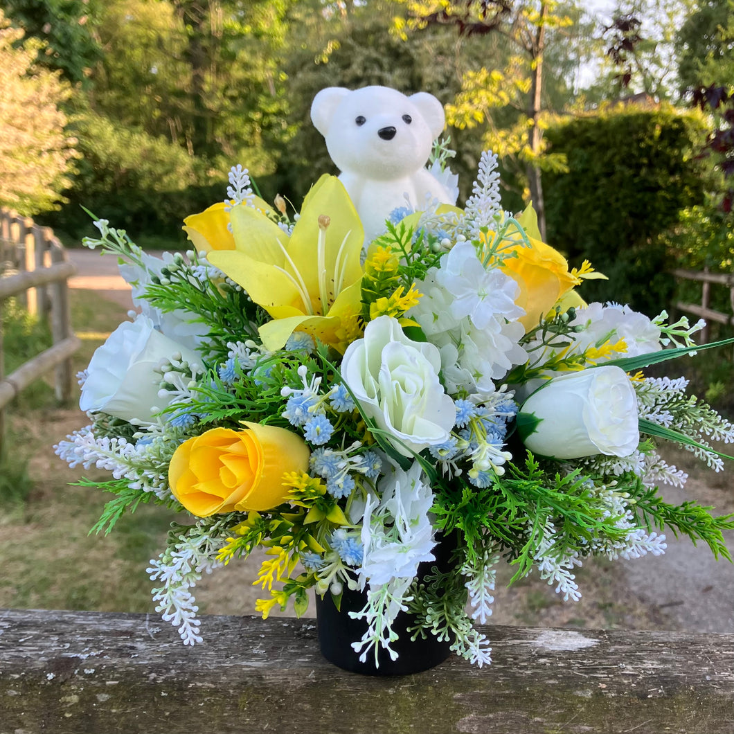 A graveside flower arrangement with teddy in black pot