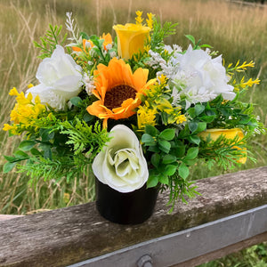 a grave side pot with flowers in shades of yellow and cream
