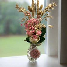 A posy of dried pink grasses and silk rose flowers in glass bud vase