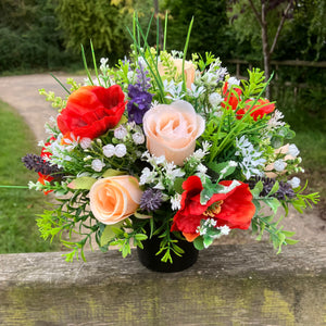 a grave pot with orange and pale purple artificial silk blooms