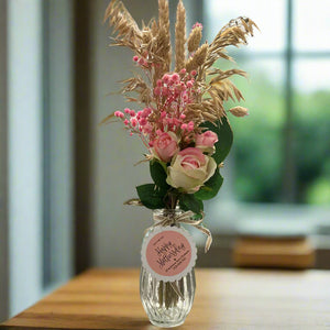 A posy of dried pink grasses and silk rose flowers in glass bud vase