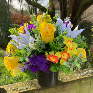 a yellow and purple graveside flower arrangement in black plastic pot