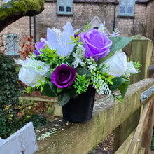 a graveside ivory and purple artificial memorial flower arrangement in black plastic pot