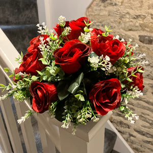 A graveside flower arrangement of roses and gyp in black pot