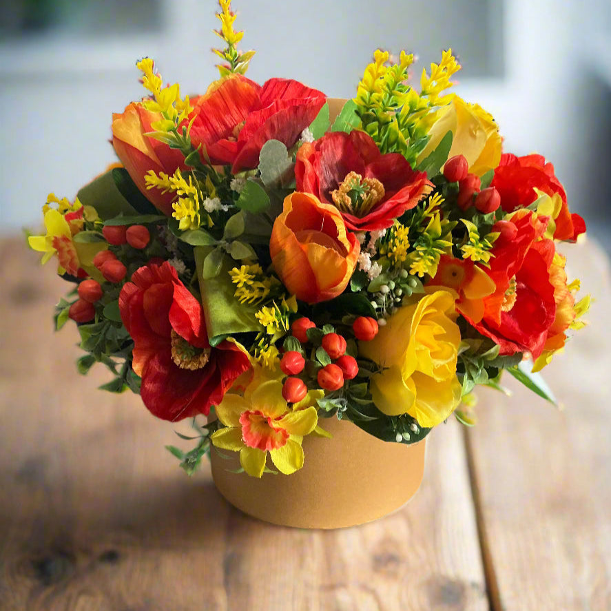 artificial tulips poppies, daffodila and berries in shades of orange and yellow in gold hat box