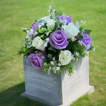 a graveside ivory and lilac artificial memorial flower arrangement in black plastic pot