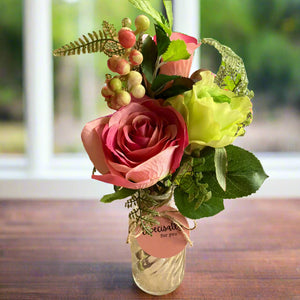 A posy of artificial pink and green flowers in glass bud vase