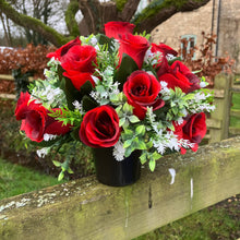 A graveside flower arrangement of roses and gyp in black pot