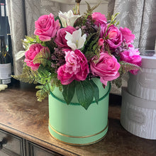 A flower arrangement of faux silk flowers in sage green hat box