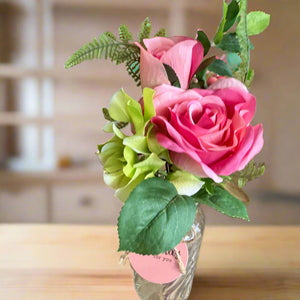 A posy of artificial pink and green flowers in glass bud vase