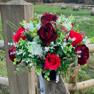 a graveside pot with a red and white artificial silk flower arrangement