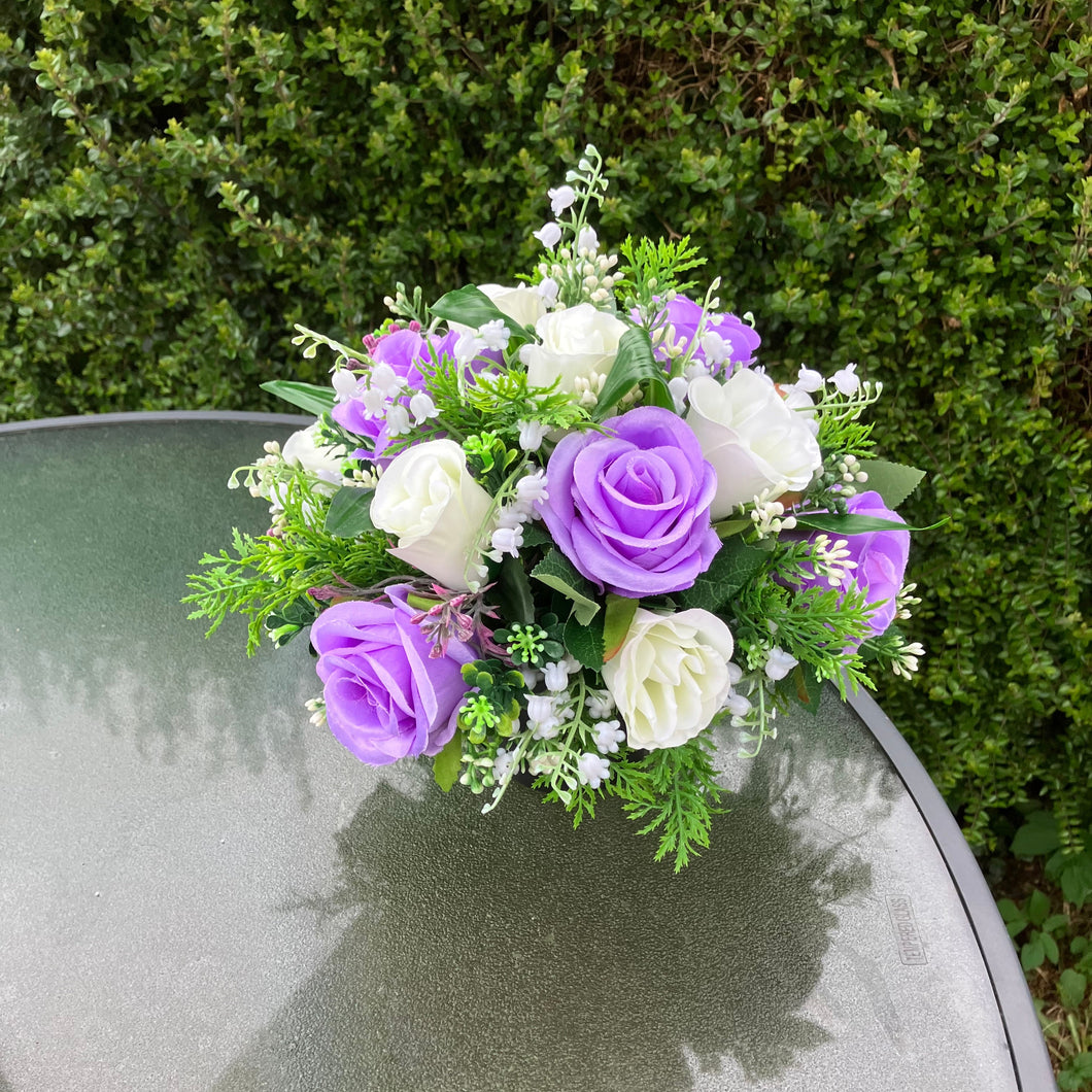 a graveside ivory and lilac artificial memorial flower arrangement in black plastic pot