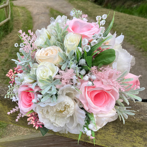 a brides wedding bouquet of artificial flowers  in shades of ivory & pink