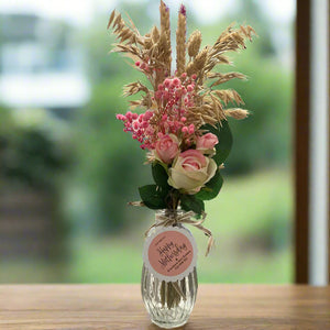 A posy of dried pink grasses and silk rose flowers in glass bud vase