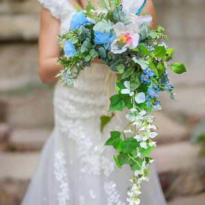 Bouquet with blue, green, and white flowers held by a person wearing a white dress.