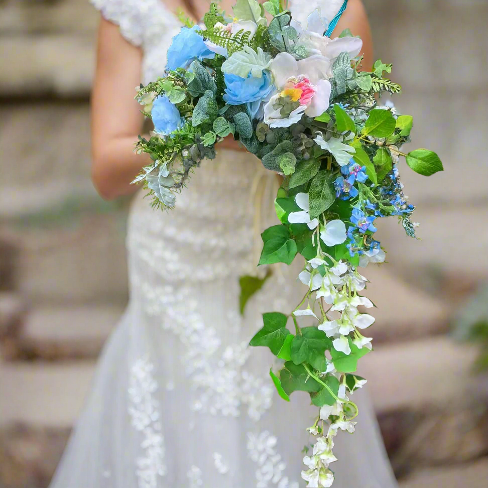 Bouquet with blue, green, and white flowers held by a person wearing a white dress.