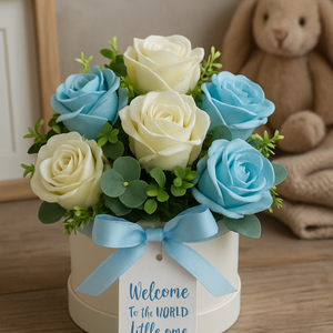 Bouquet of blue and white roses with a baby shower message tag, placed on a wooden surface.