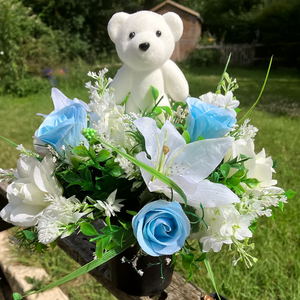 a cream and blue graveside flower arrangement in black plastic pot