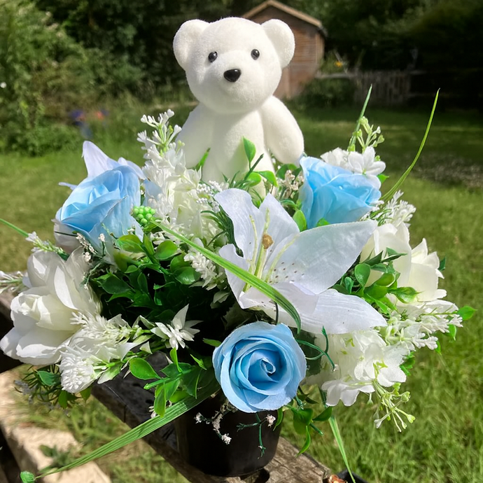 a cream and blue graveside flower arrangement in black plastic pot