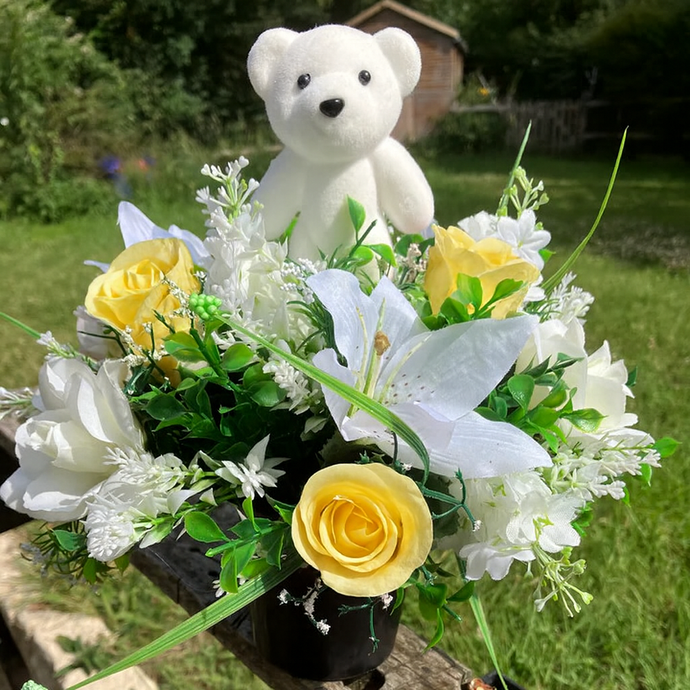 A graveside flower arrangement with teddy in black pot
