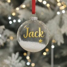 Clear Christmas ornament with 'Jack' and a star, hanging on a tree with blurred lights in the background.