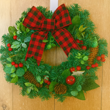 Christmas wreath with a red and green checkered bow on a wooden door.