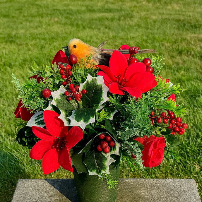 Bouquet of red flowers and greenery with a bird on a stone pedestal against a grassy background