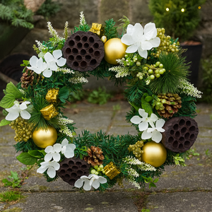 Decorative wreath with flowers, pinecones, and gold balls against a stone wall.