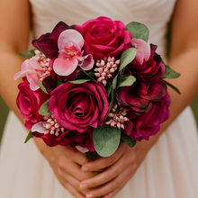 Bouquet of pink and red flowers held by a person wearing a white dress.