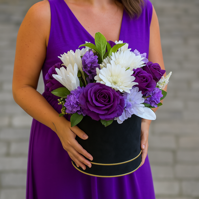 Person wearing a purple dress holding a bouquet of purple and white flowers in a black box.