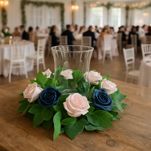 Decorative floral arrangement with blue and pink roses on a wooden table, blurred wedding reception in the background.