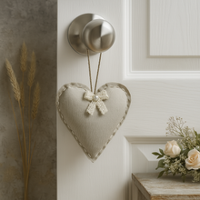 Heart-shaped decorative item with a bow hanging on a wall next to a window and flowers.