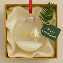 Christmas ornament with 'name' and a star, tied with a green tag reading 'Merry Christmas', in a gold box.