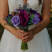 Bouquet of purple and green flowers held by a person in a white dress.