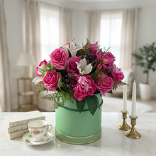 A flower arrangement of faux silk flowers in sage green hat box