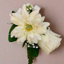 an artificial wedding corsage featuring a rose and gerbera with foliage