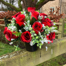 A graveside flower arrangement of roses and gyp in black pot