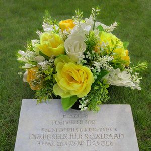 a grave side pot with flowers in shades of yellow and cream