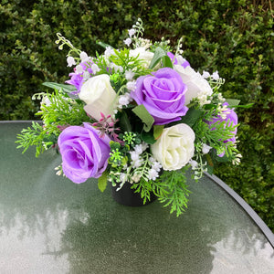 a graveside ivory and lilac artificial memorial flower arrangement in black plastic pot