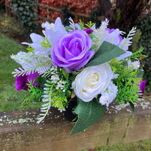 a graveside ivory and purple artificial memorial flower arrangement in black plastic pot