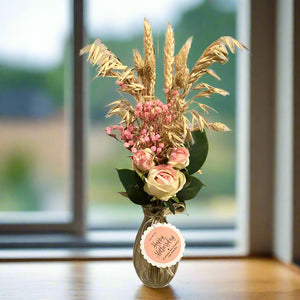 A posy of dried pink grasses and silk rose flowers in glass bud vase